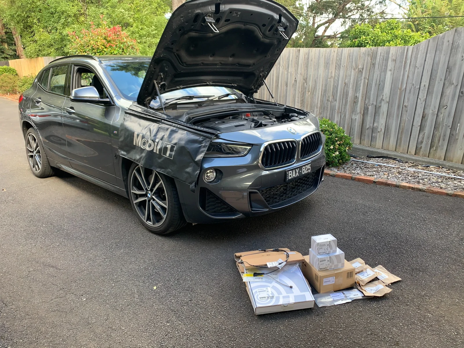 BMW X2 front-end maintenance with Mobil 1 fender cover and genuine BMW parts ready for installation