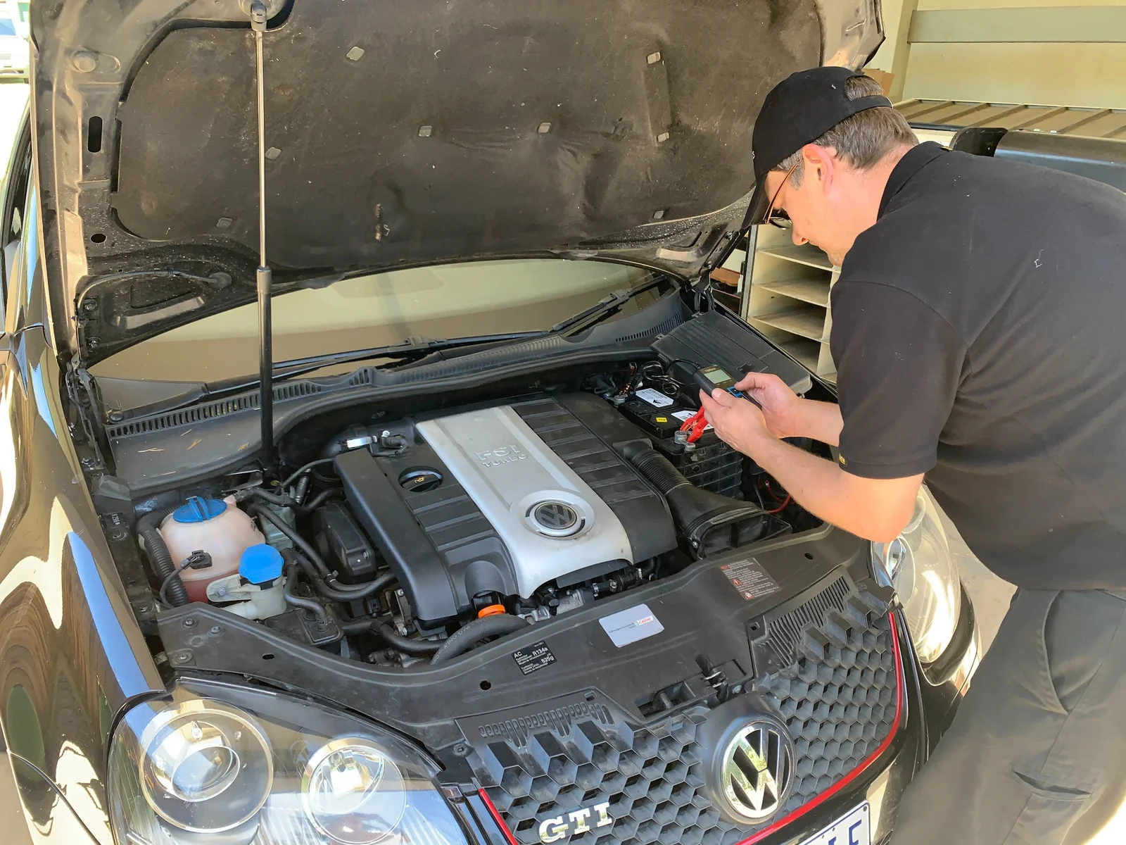Mechanic inspecting and testing the battery of a Volkswagen GTI with hood open